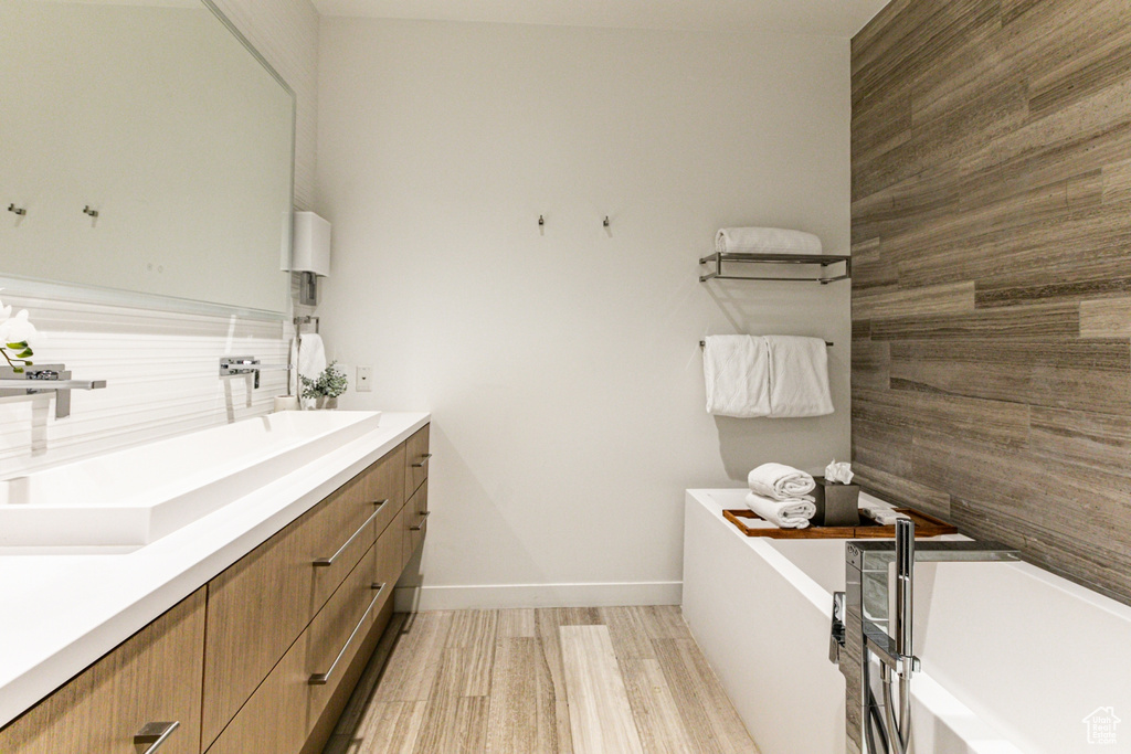 Bathroom featuring vanity, wood-type flooring, a bath, and tasteful backsplash