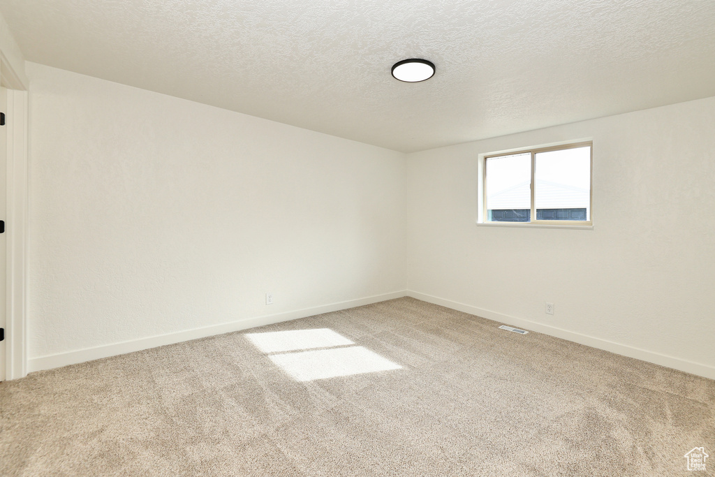 Empty room featuring a textured ceiling and light colored carpet