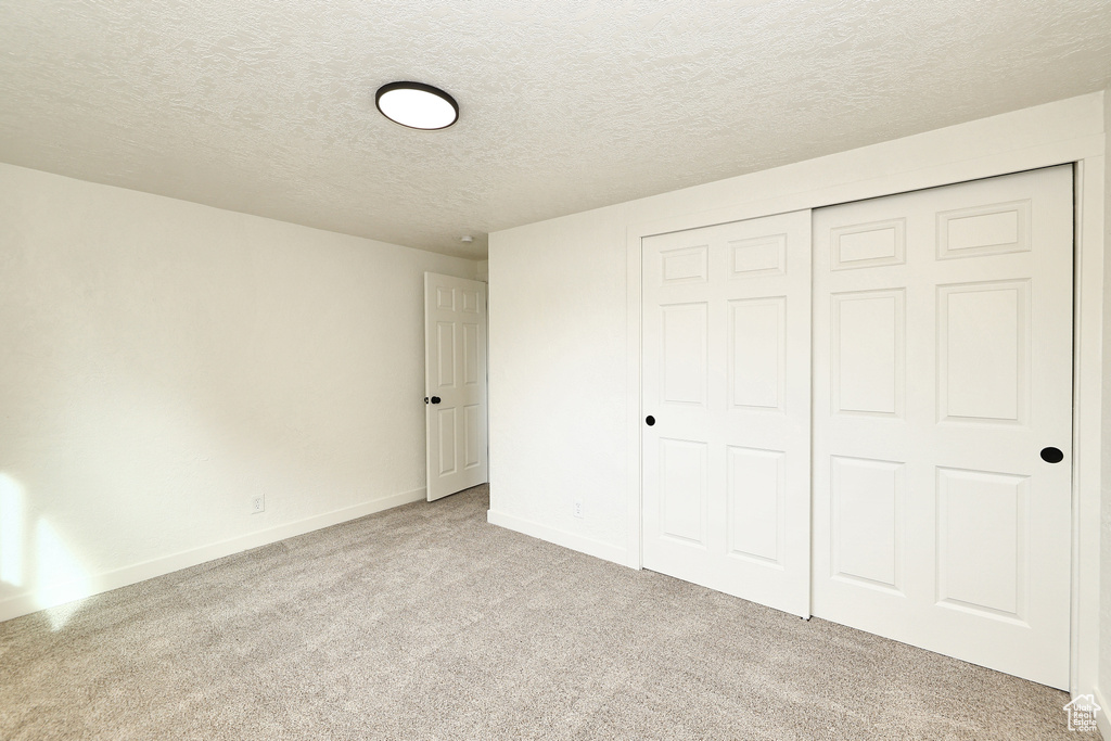 Unfurnished bedroom featuring light carpet, a textured ceiling, and a closet