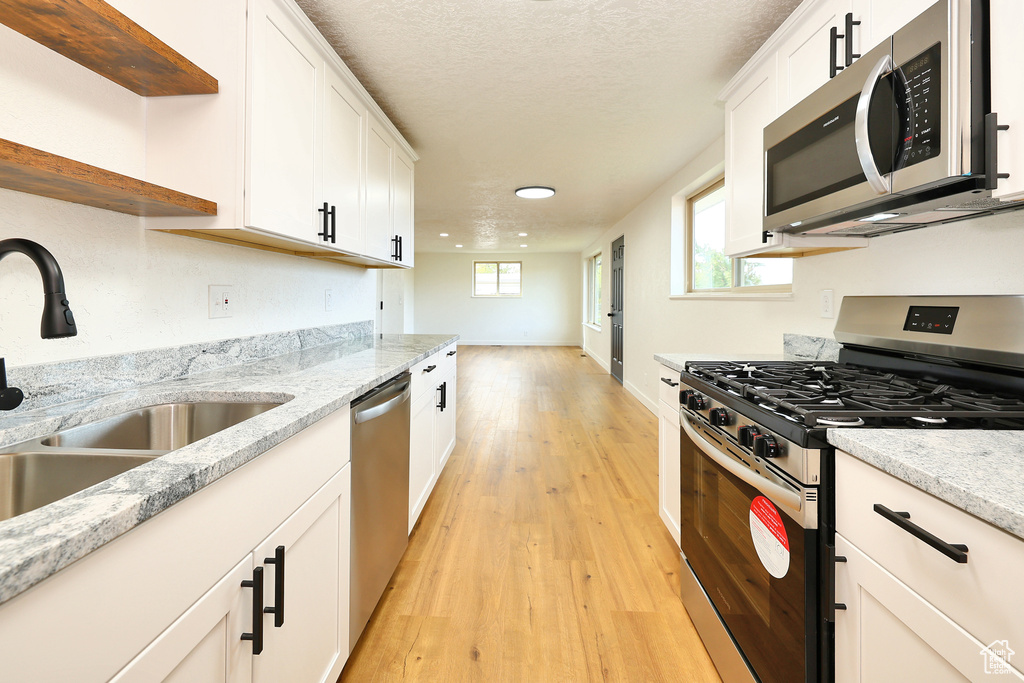 Kitchen with sink, appliances with stainless steel finishes, white cabinetry, and light hardwood / wood-style floors