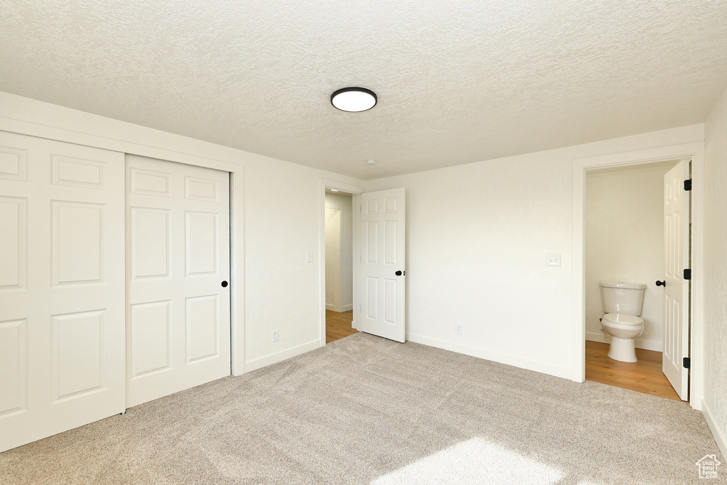 Unfurnished bedroom with a closet, light carpet, a textured ceiling, and ensuite bath