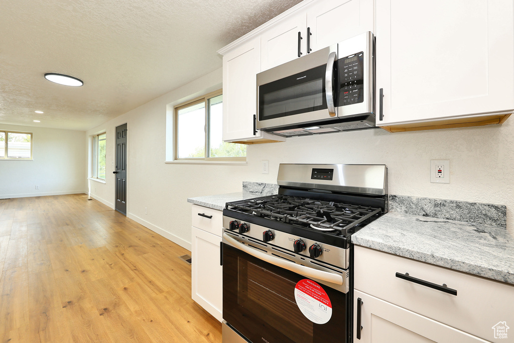 Kitchen featuring appliances with stainless steel finishes, white cabinetry, light stone countertops, a textured ceiling, and light hardwood / wood-style flooring