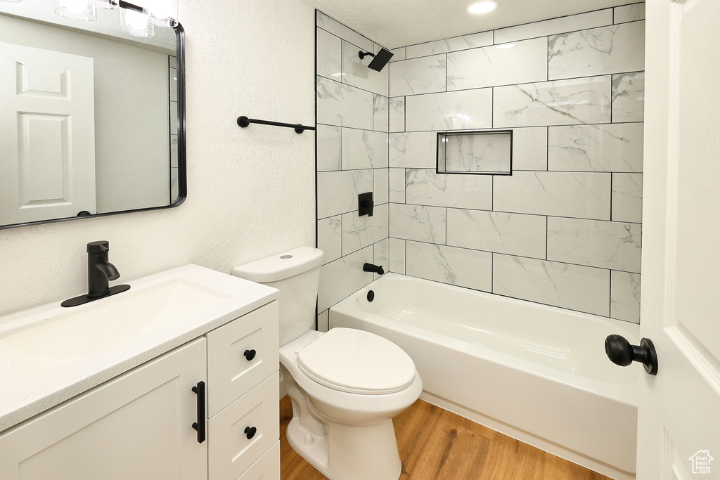 Full bathroom with vanity, toilet, tiled shower / bath combo, and wood-type flooring