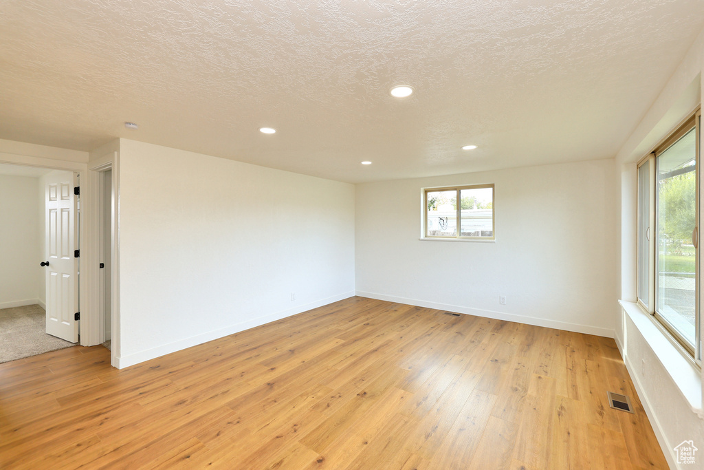 Unfurnished room featuring light hardwood / wood-style floors, a textured ceiling, and a healthy amount of sunlight