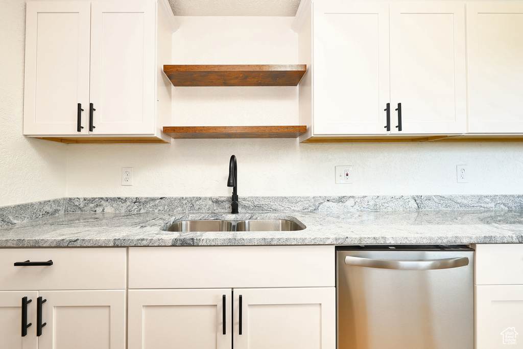 Kitchen with stainless steel dishwasher, sink, and light stone counters