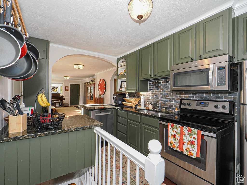 Kitchen with kitchen peninsula, decorative backsplash, appliances with stainless steel finishes, dark stone counters, and green cabinetry