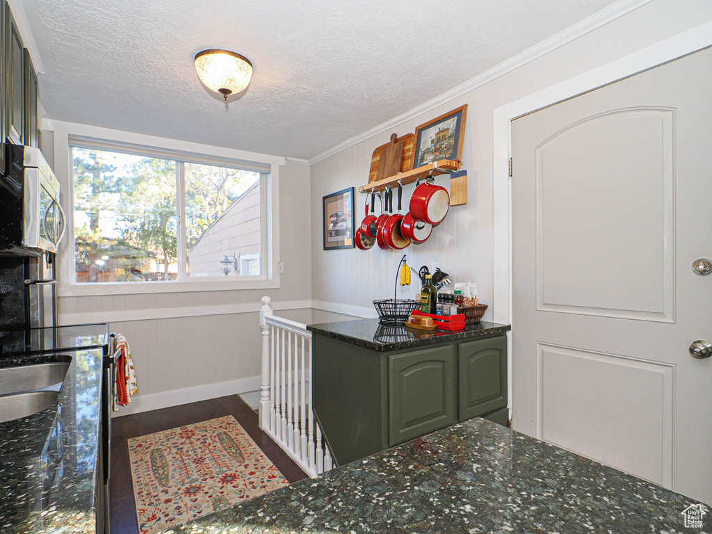 Interior space featuring dark wood-type flooring, dark stone counters, ornamental molding, green cabinetry, and a textured ceiling