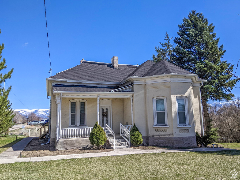 View of front of home with brick siding, covered porch, a front lawn, and a chimney
