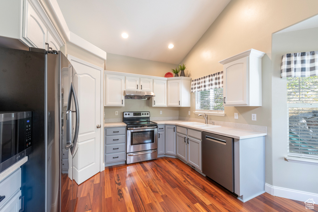 Kitchen with dark hardwood / wood-style flooring, white cabinets, stainless steel appliances, and vaulted ceiling