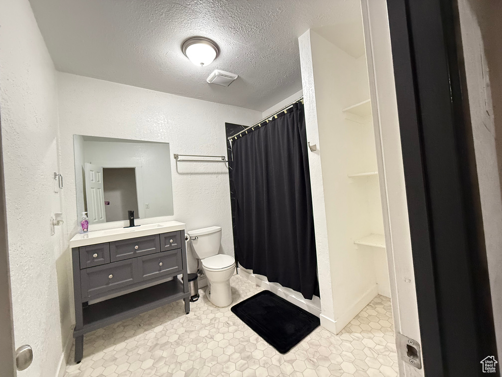 Bathroom featuring toilet, a textured ceiling, curtained shower, and vanity