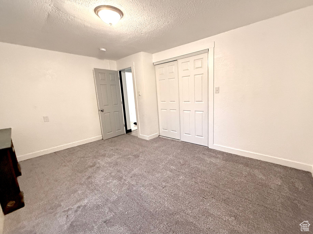 Unfurnished bedroom featuring a closet, a textured ceiling, and dark colored carpet