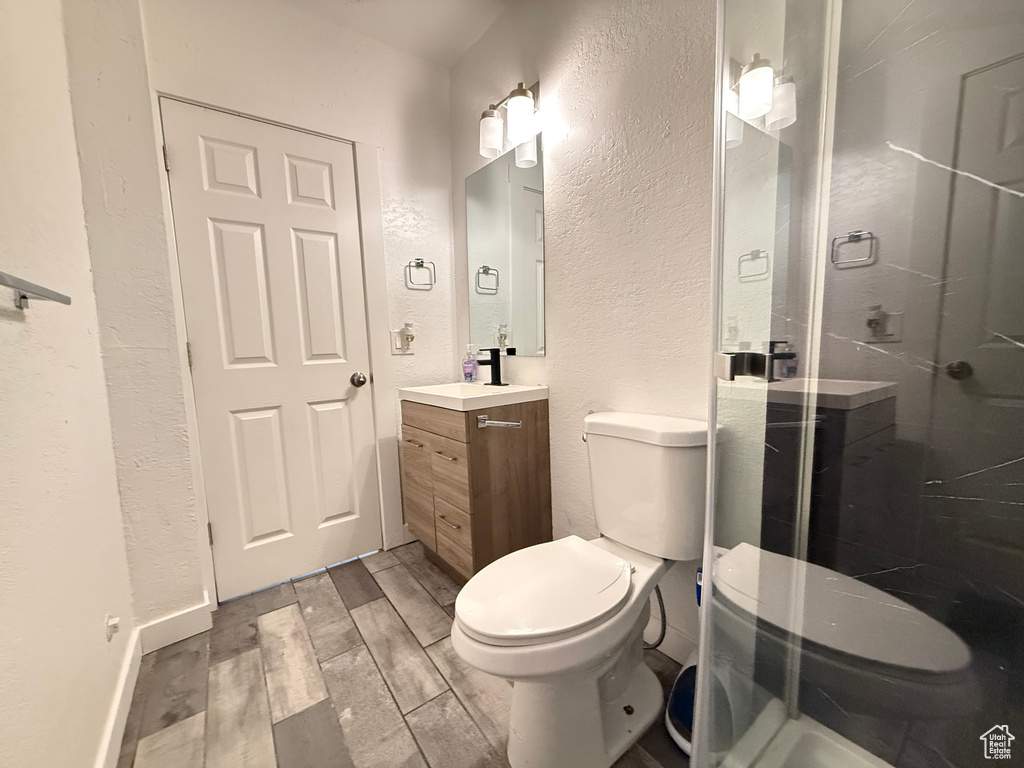 Bathroom featuring vanity, hardwood / wood-style floors, a shower with shower door, and toilet