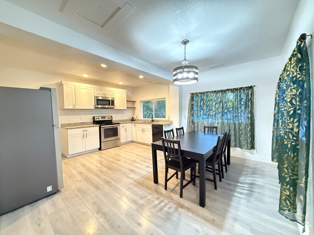 Dining area with an inviting chandelier, a textured ceiling, and light wood-type flooring