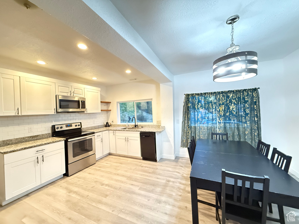 Kitchen with white cabinets, light hardwood / wood-style floors, stainless steel appliances, and hanging light fixtures