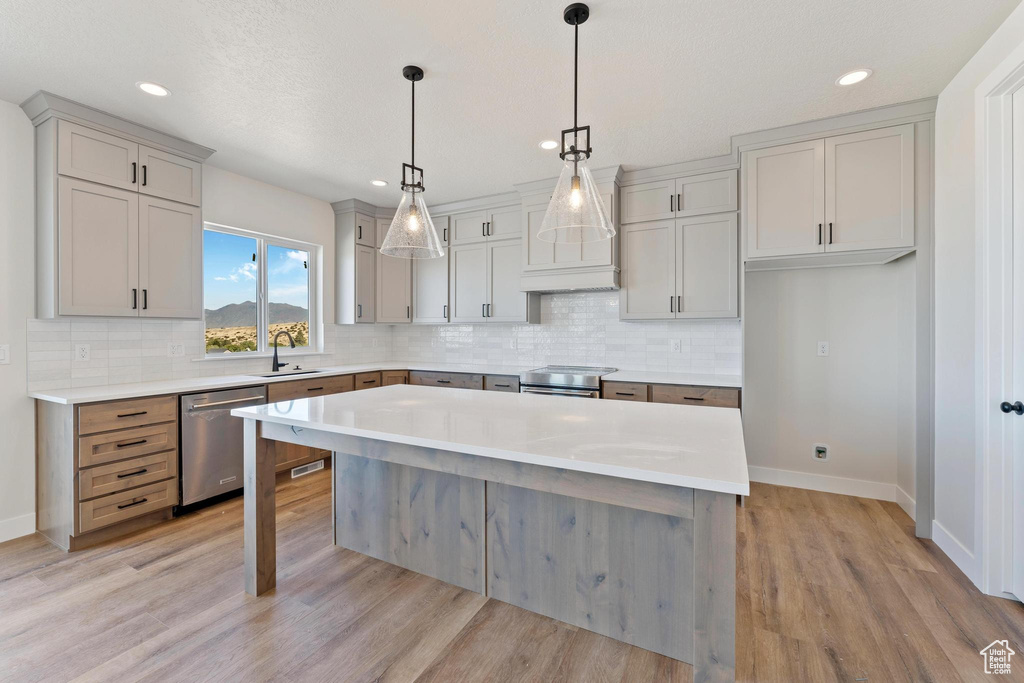 Kitchen featuring appliances with stainless steel finishes, sink, a center island, decorative light fixtures, and light hardwood / wood-style flooring