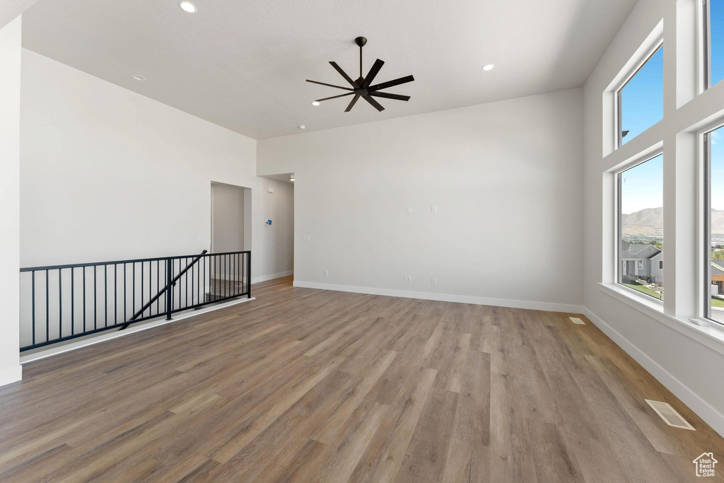 Unfurnished room featuring a mountain view, ceiling fan, a towering ceiling, and light hardwood / wood-style flooring