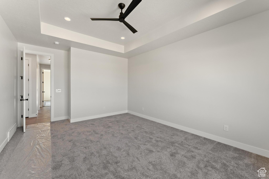 Empty room featuring carpet, ceiling fan, and a raised ceiling