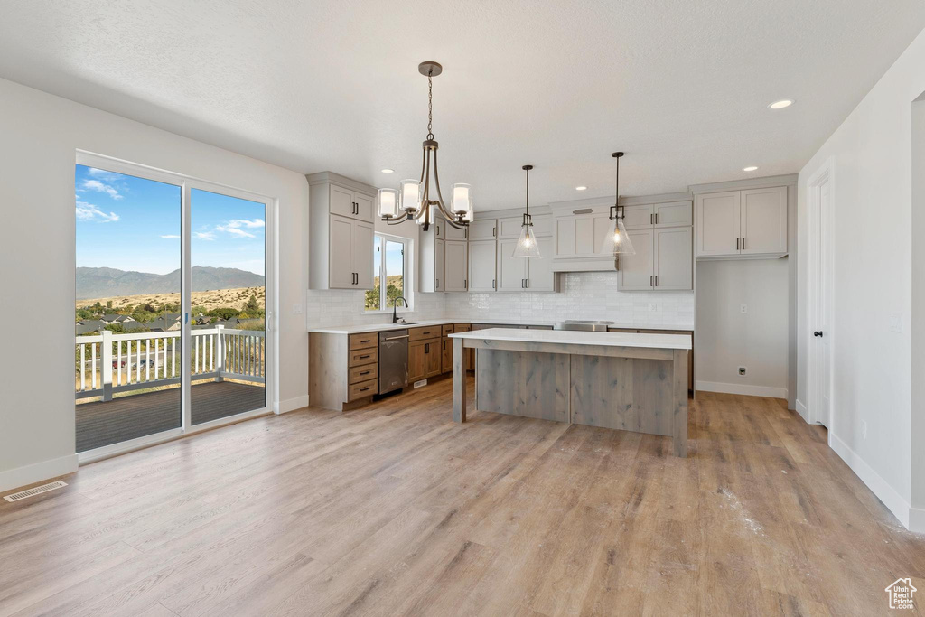 Kitchen with dishwasher, a kitchen island, hanging light fixtures, a mountain view, and light hardwood / wood-style flooring