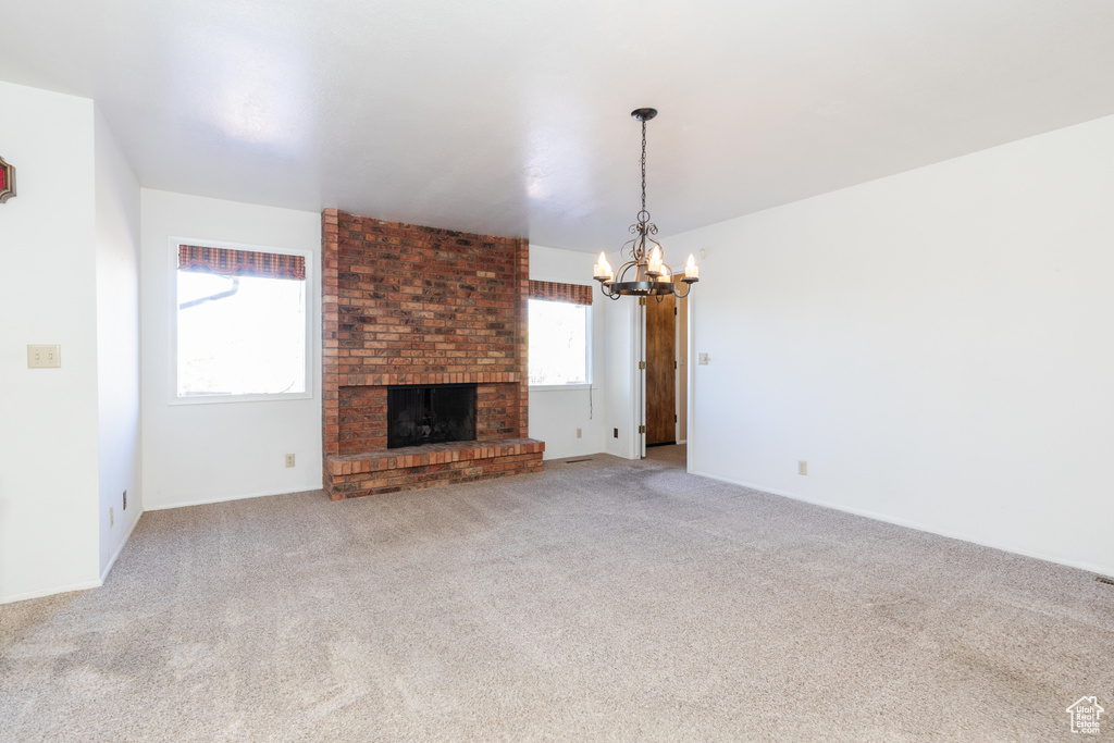 Unfurnished living room with an inviting chandelier, carpet flooring, and a fireplace