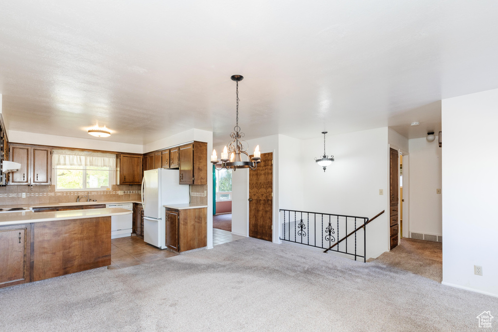 Kitchen with white appliances, sink, backsplash, decorative light fixtures, and light colored carpet