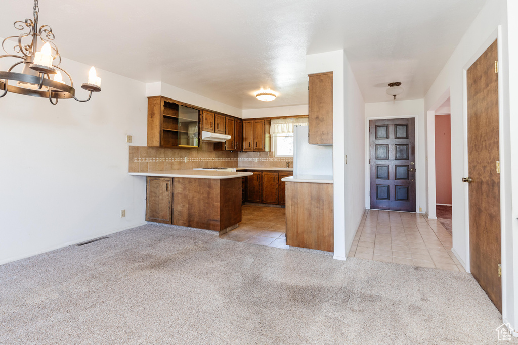 Kitchen featuring kitchen peninsula, backsplash, pendant lighting, white fridge, and light colored carpet