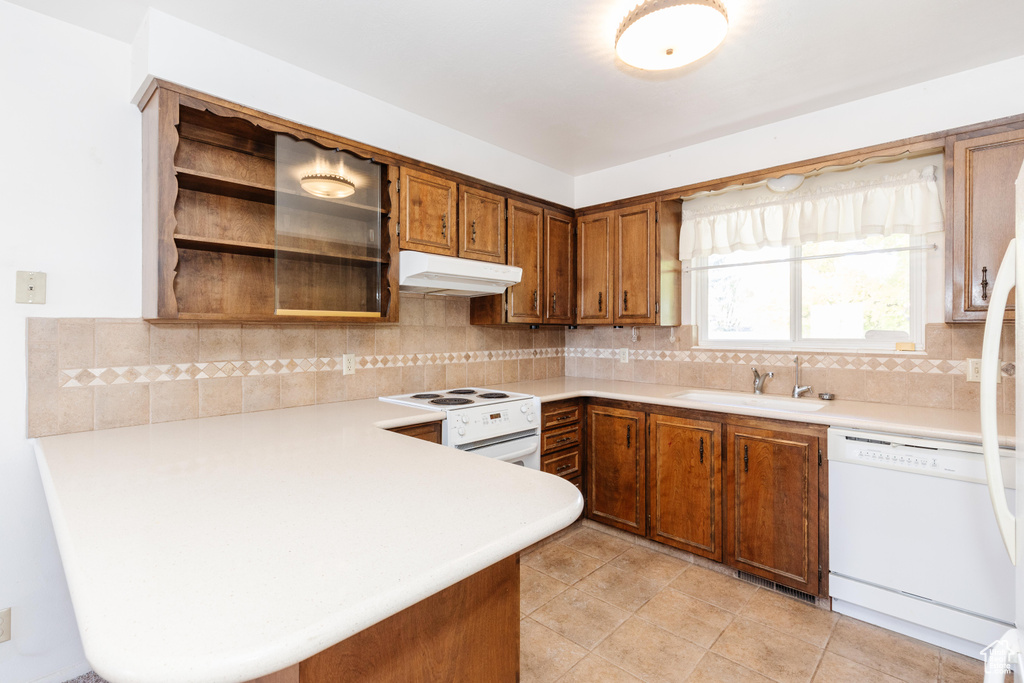 Kitchen featuring kitchen peninsula, light tile patterned floors, backsplash, sink, and white appliances