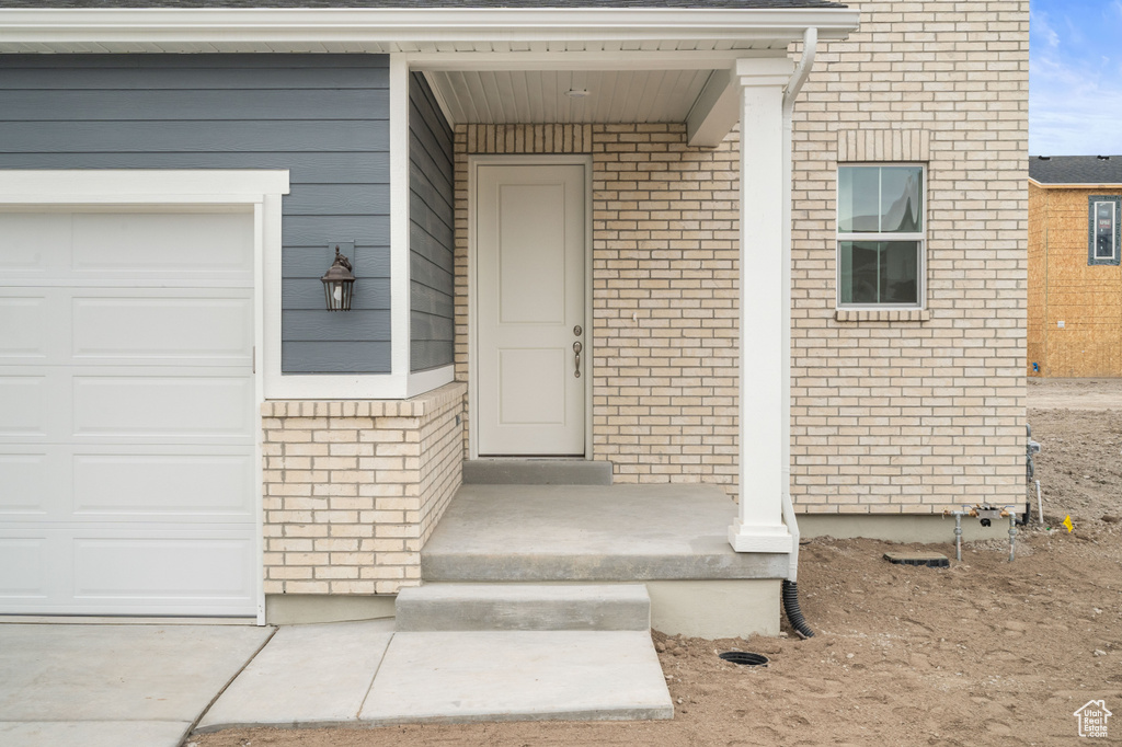View of exterior entry with an attached garage and brick siding