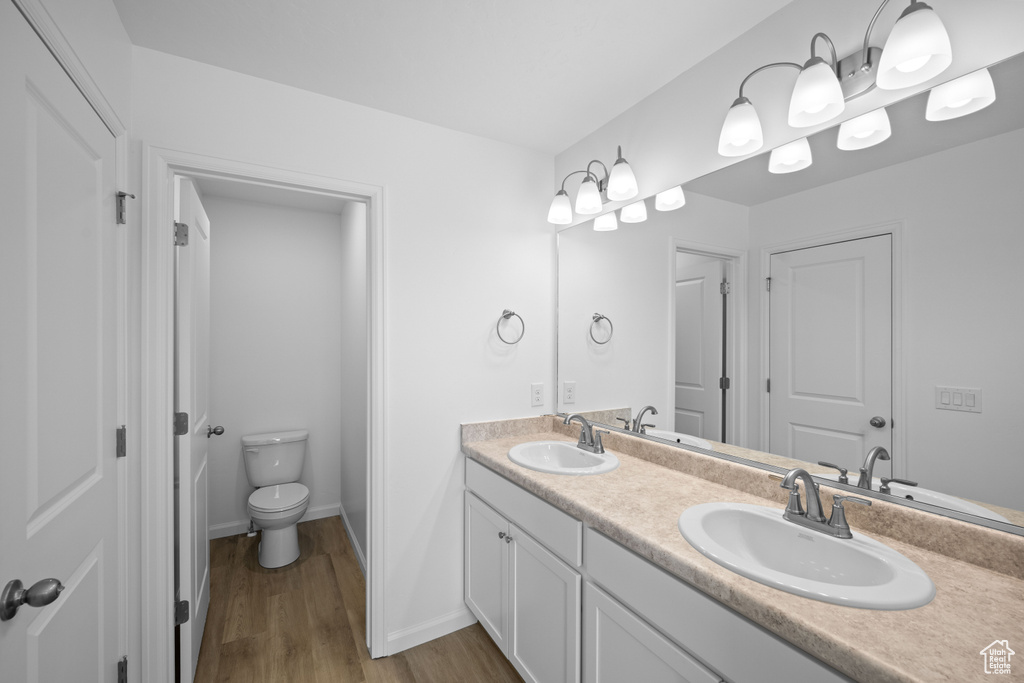 Full bathroom with double vanity, wood finished floors, toilet, and baseboards