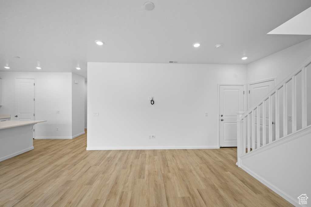 Unfurnished living room with recessed lighting, light wood-type flooring, baseboards, and stairs