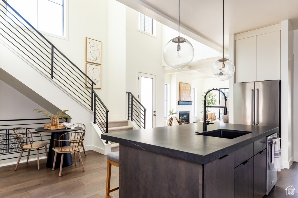 Kitchen featuring dark hardwood / wood-style floors, high end fridge, hanging light fixtures, sink, and white cabinets