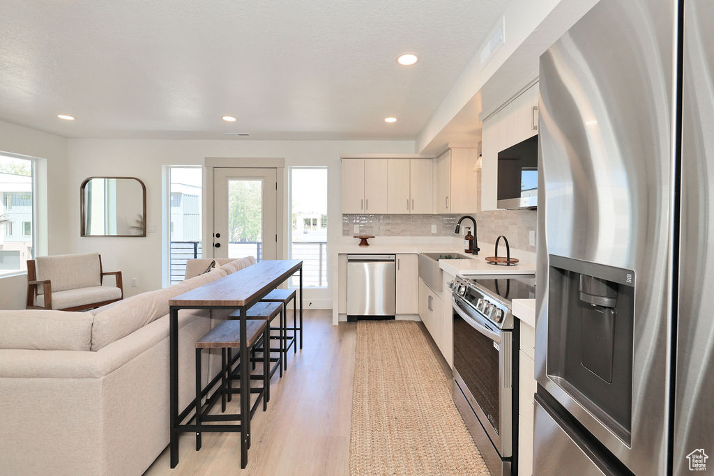 Kitchen with stainless steel appliances, light wood finished floors, light countertops, recessed lighting, and open floor plan
