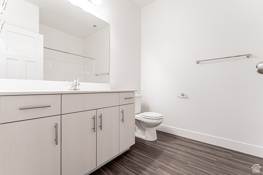 Full bathroom featuring baseboards, wood finished floors, toilet, and vanity