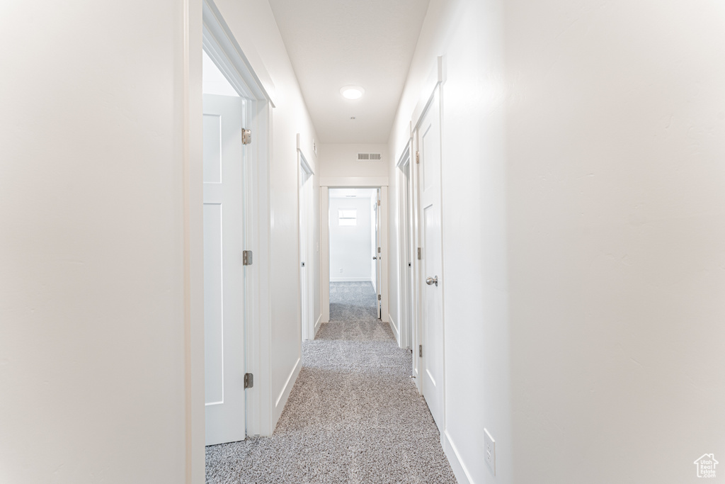 Hall with baseboards, visible vents, and light colored carpet