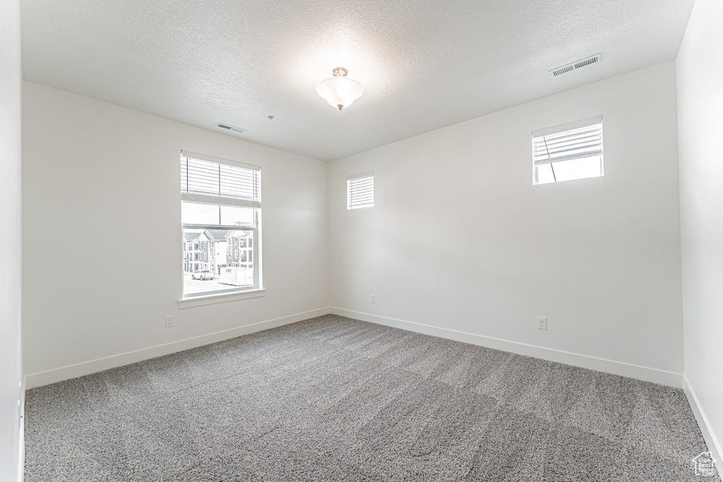 Spare room with baseboards, carpet floors, a textured ceiling, and visible vents