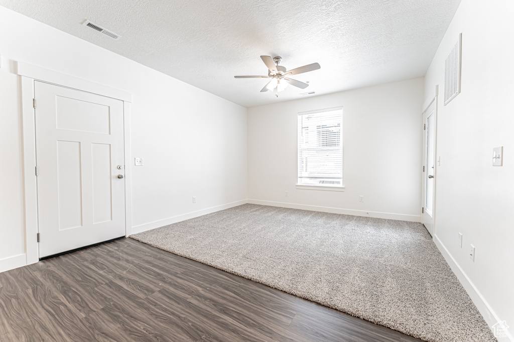 Empty room with a textured ceiling, visible vents, a ceiling fan, and wood finished floors