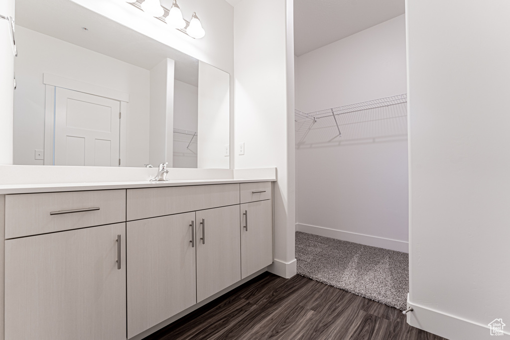 Bathroom with a spacious closet, vanity, baseboards, and wood finished floors