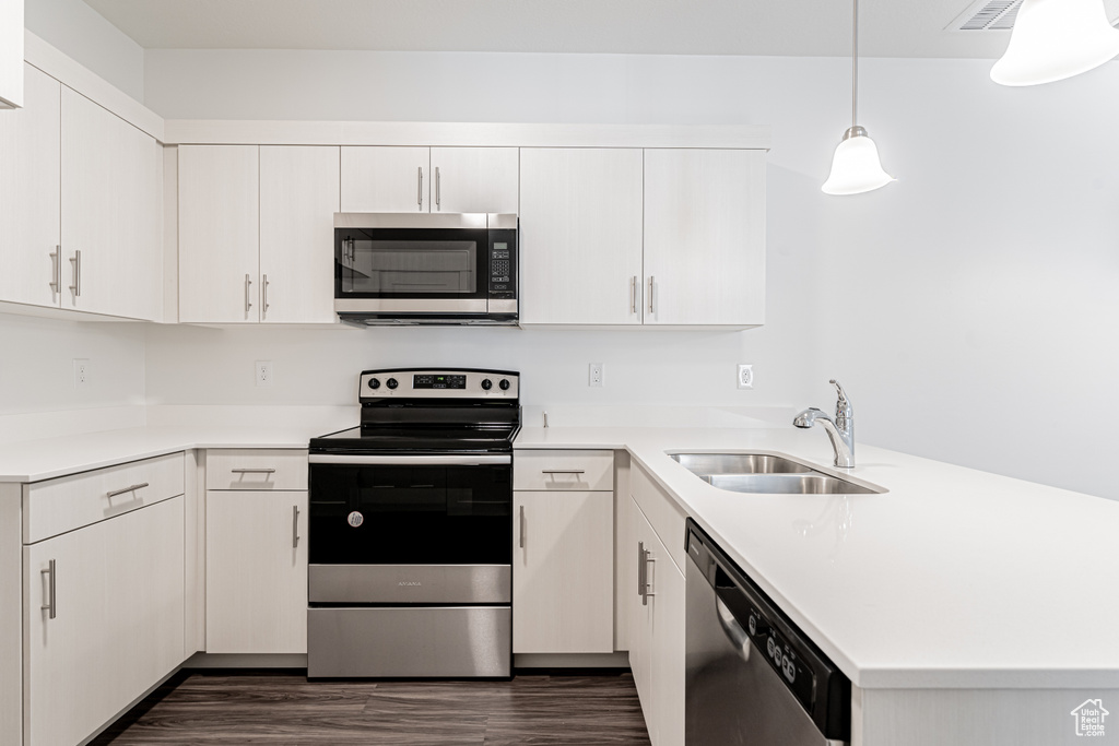 Kitchen with light countertops, dark wood-style flooring, a sink, a peninsula, and appliances with stainless steel finishes