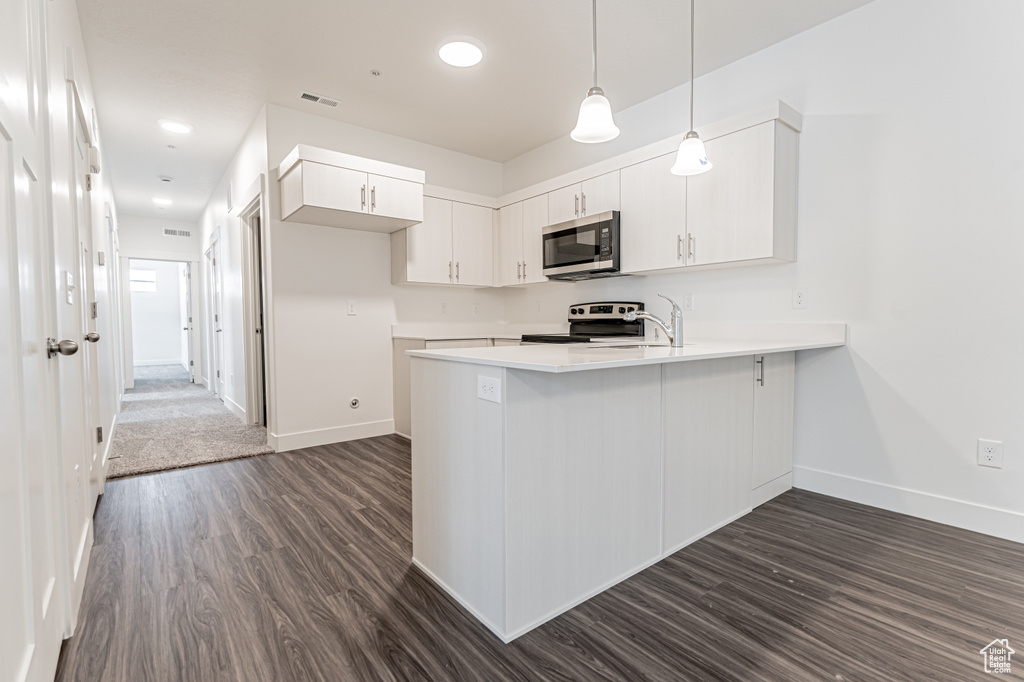 Kitchen with light countertops, appliances with stainless steel finishes, a peninsula, visible vents, and dark wood-type flooring