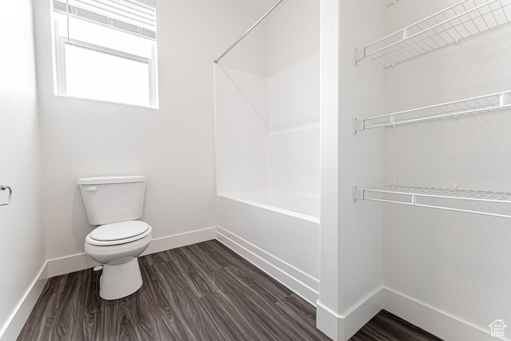 Bathroom featuring baseboards, shower / washtub combination, toilet, and wood finished floors