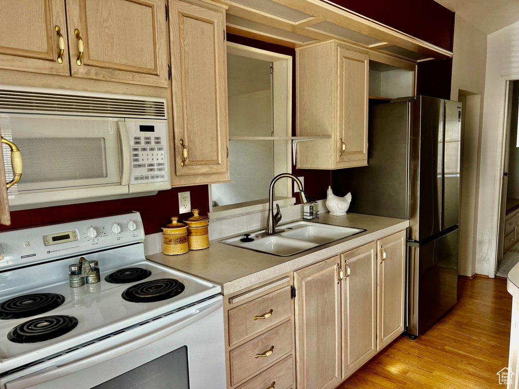 Kitchen featuring light brown cabinets, light wood-type flooring, light countertops, white appliances, and a sink