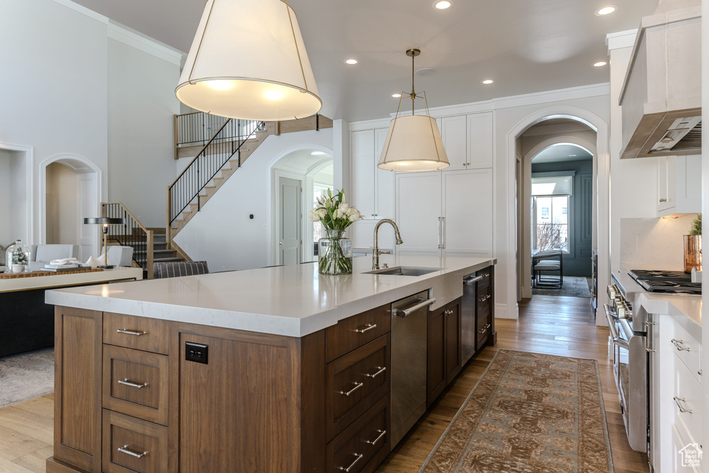 Kitchen featuring wall chimney range hood, hanging light fixtures, white cabinetry, wood-type flooring, and stainless steel appliances