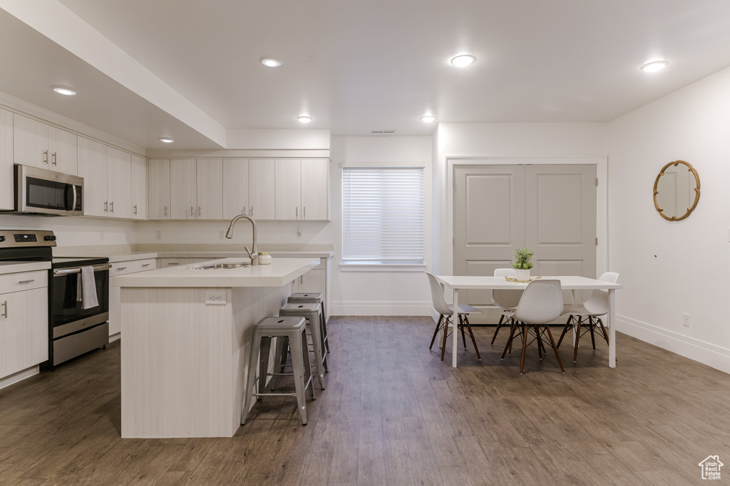 Kitchen with appliances with stainless steel finishes, white cabinets, dark wood-type flooring, a breakfast bar, and a kitchen island with sink