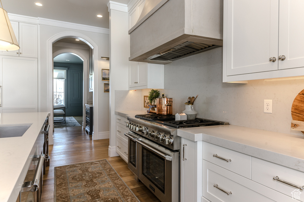 Kitchen with wall chimney range hood, white cabinets, ornamental molding, dark wood-type flooring, and range with two ovens