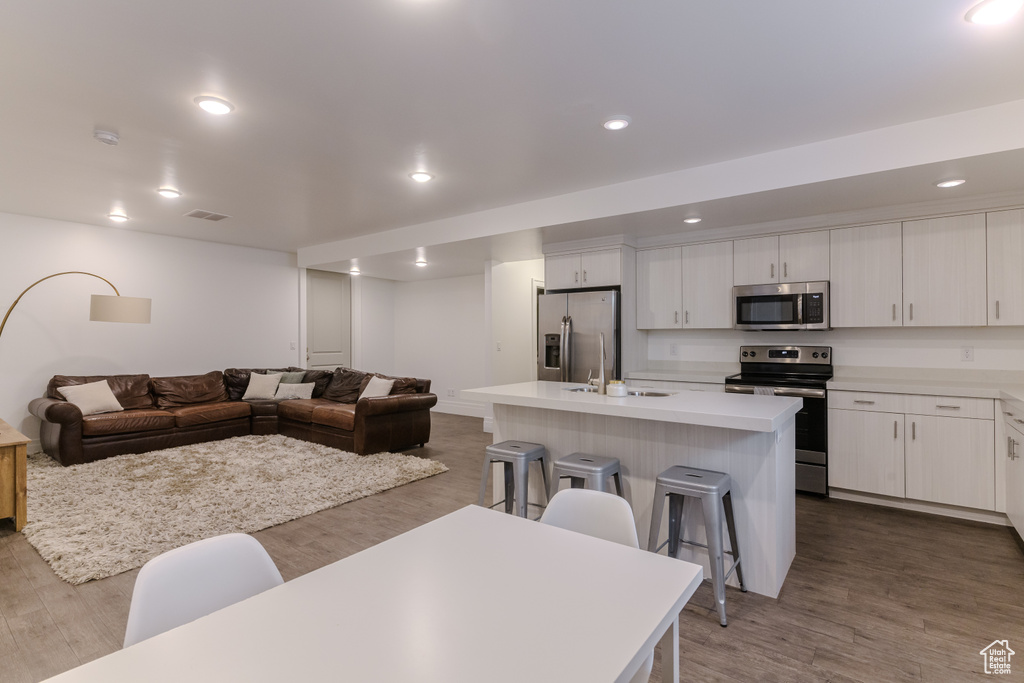 Kitchen featuring a kitchen breakfast bar, stainless steel appliances, white cabinets, hardwood / wood-style flooring, and a center island with sink