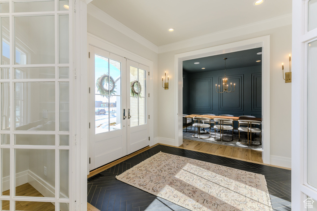 Entryway with french doors, dark parquet floors, ornamental molding, and a chandelier