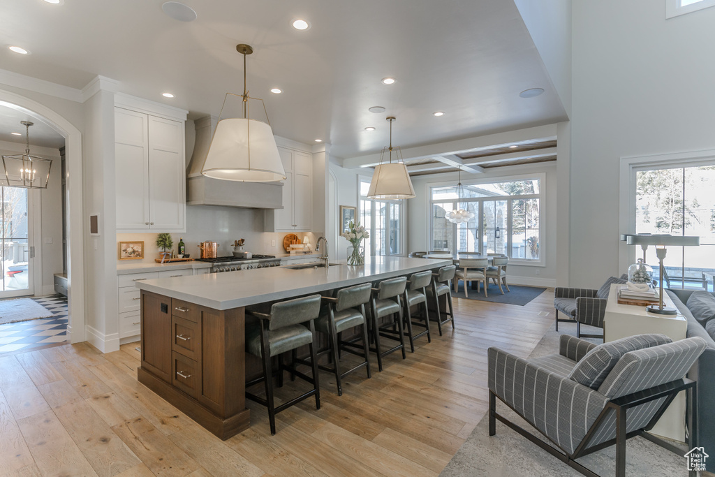 Kitchen with white cabinetry, decorative light fixtures, a center island with sink, and light wood-type flooring