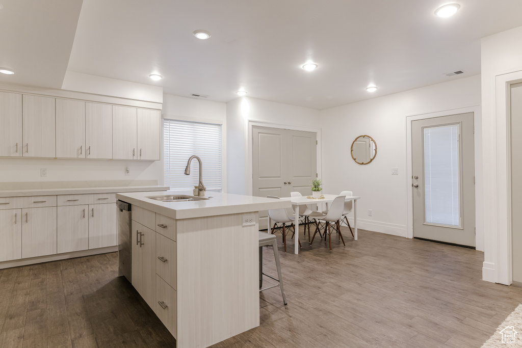 Kitchen featuring a center island with sink, a kitchen breakfast bar, stainless steel dishwasher, light wood-type flooring, and sink