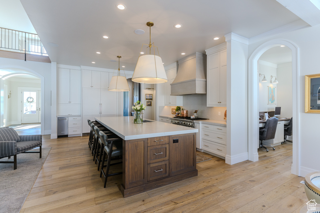 Kitchen with custom exhaust hood, a center island, white cabinetry, and light hardwood / wood-style floors