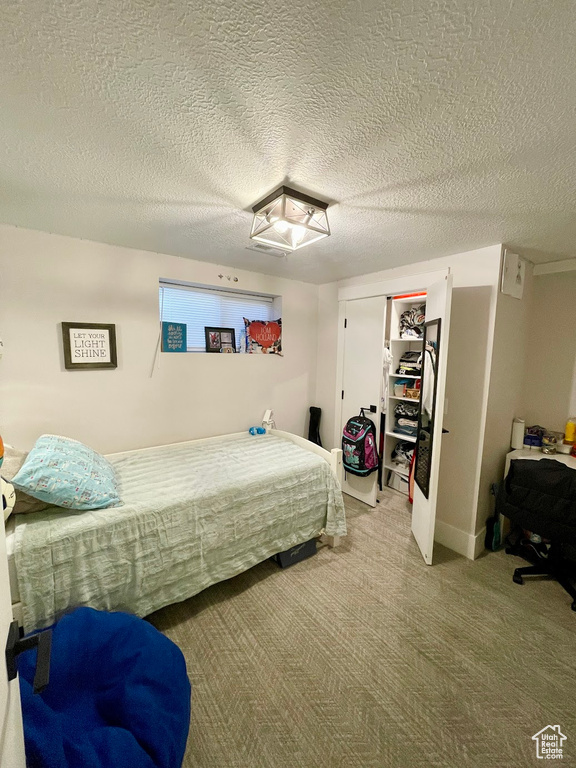 Carpeted bedroom featuring a textured ceiling, a walk in closet, and a closet