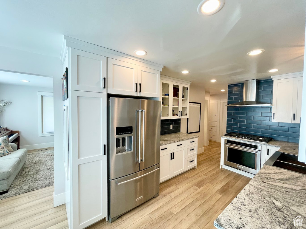 Kitchen with white cabinets, light hardwood / wood-style floors, wall chimney exhaust hood, and high quality appliances